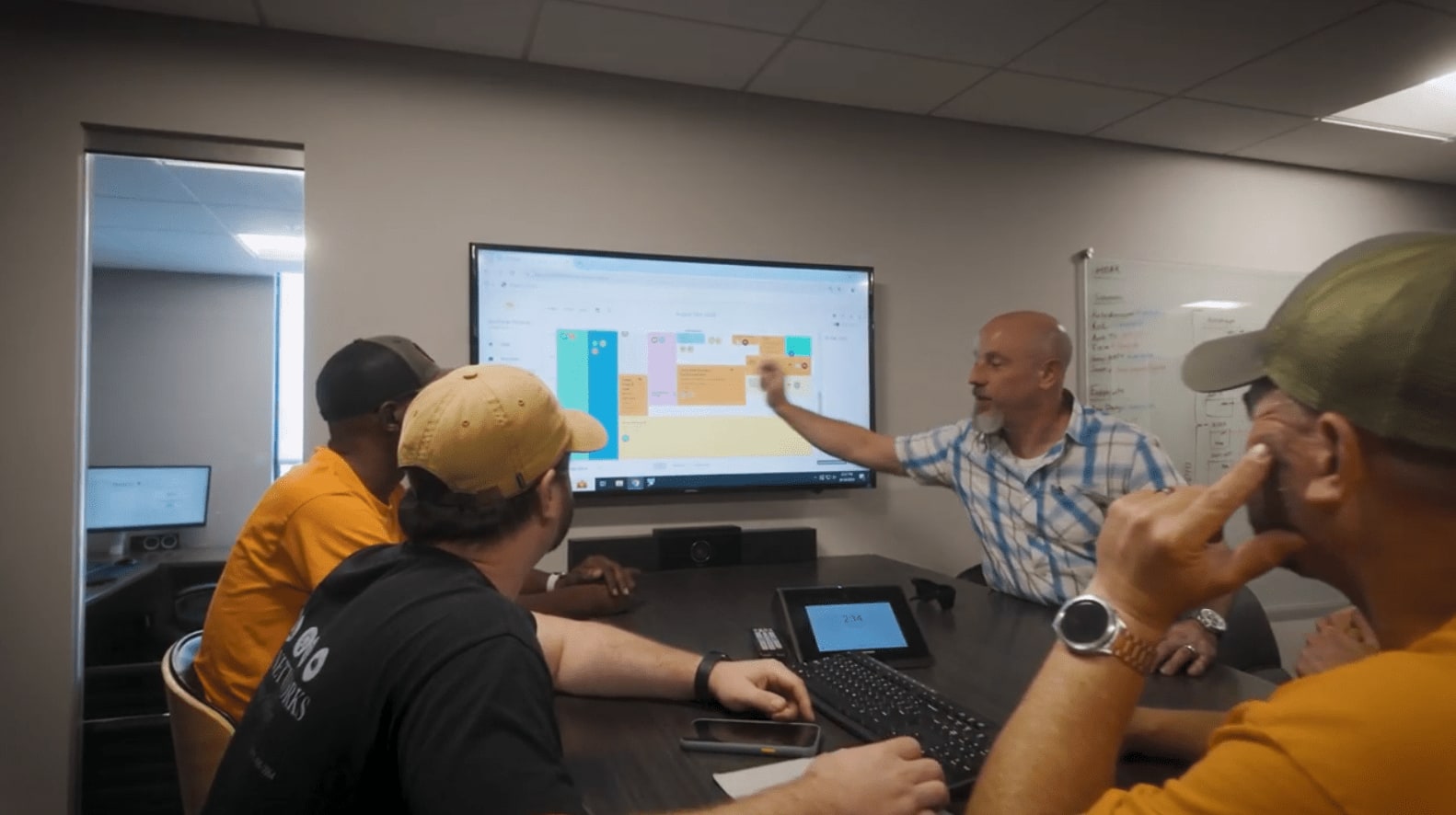 ABE Networks team in a meeting room reviewing a schedule on a wall-mounted screen